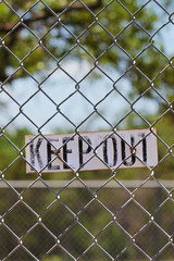 Keep Out sign on a chain link fence outside with natural tree and blue sky park in background indicating privacy ownership territory laws