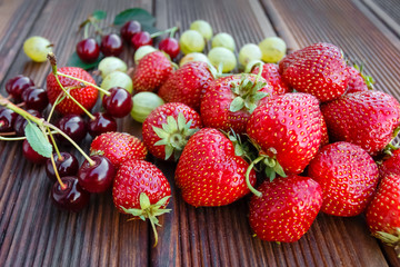 Mix of fresh and juicy berries in the summer garden on wooden texture background