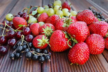 Mix of fresh and juicy berries in the summer garden on wooden texture background