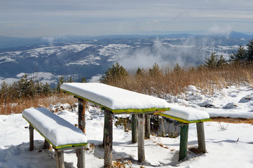 Snow covered two old wooden benches and a table, sunny winter day in Vitosha Mountain, wide panoramic views