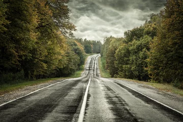 Fotobehang Donkere asfaltweg onder een stormhemel © George Dolgikh