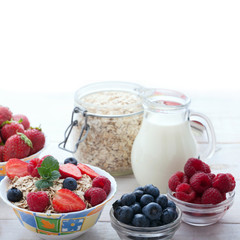 Berries, strawberries, raspberries, currants, blackberries, blueberries, nuts, milk and muesli  ingredients for healthy breakfast  on white wooden table.