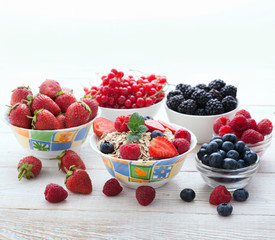 Berries, strawberries, raspberries, currants, blackberries, blueberries, nuts, milk and muesli  ingredients for healthy breakfast  on white wooden table.