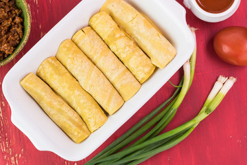 Casserole dish with mexican food - uncooked beef enchiladas and ingredients.