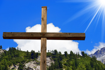 Fototapeta premium Christian Cross in Mountain / Wooden christian cross in mountain, Italian Alps, with blue sky, clouds and sun rays