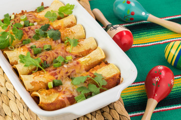 Casserole dish with mexican food - beef enchiladas and fiesta colorful maracas.