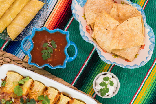 Mexican fiesta table. Beef enchiladas dish, salsa, chips, sour cream.
