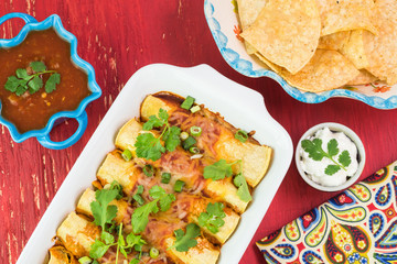 Mexican fiesta table. Beef enchiladas dish, salsa, chips, sour cream.