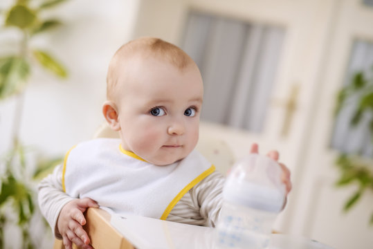 Baby boy sitting in high chair and holding a bottle