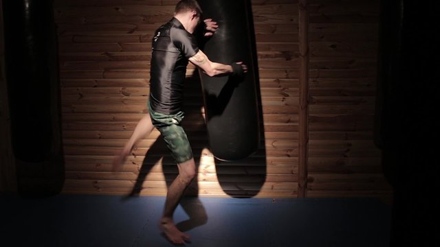 Молодой человек тренируется с боксерской грушей в зале смешанных единоборств.