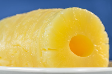 Slices of canned pineapple preserved at its own juice, on oval dish and blue background
