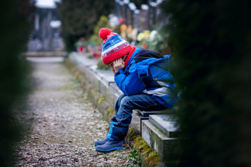 Sad little boy, sitting on a grave in a cemetery