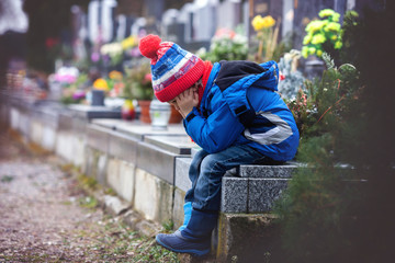 Sad little boy, sitting on a grave in a cemetery
