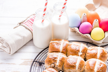 Hot cross bun on tray with Easter vibrant eggs and milk.