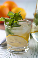 Glass of detox drink water with mineral water, lemon slices and mint on wooden table. Drink for diet. Focus on mint.