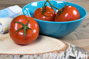 Whole fresh tomatoes in/near blue bowl on wooden background.
Cooking concept.