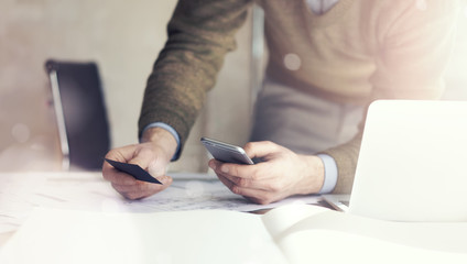 Businessman holding hand businesscard and making photo smartphone. Architectural project on the table. Horizontal mockup. Blurred, bokeh effect