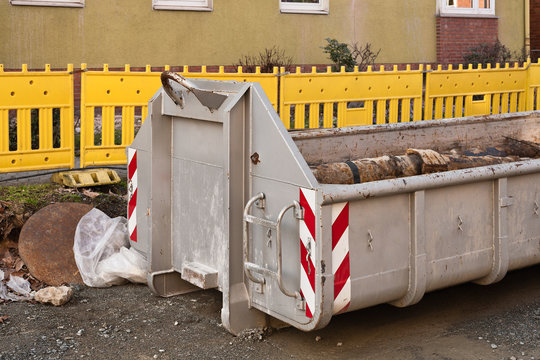 Ein grosser grauer Rollcontainer f&uuml;r Bauschutt vor gelben Baken
