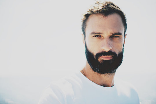 Young bearded guy wearing white blank t-shirt and looking on the camera in sunny day. Horizontal