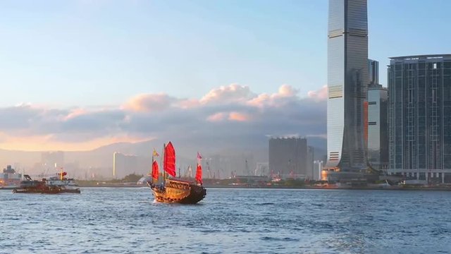 Red sail traditional junk boat in Hong Kong harbor and urban Asia architecture