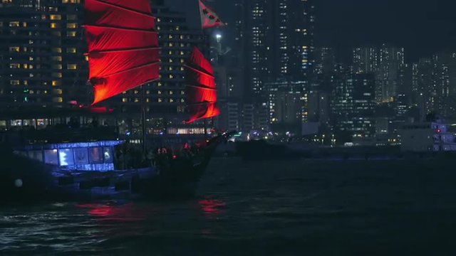 Hong Kong tourist tour boat with red sails at night in Victoria harbor