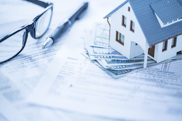 Miniature house with money on tax papers