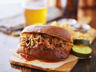 pulled pork sandwich on wooden tray with pickles and beer