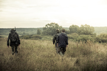 groupe de personnes qui monte tôt le matin dans un champ rural à travers les hautes herbes pendant la chasse