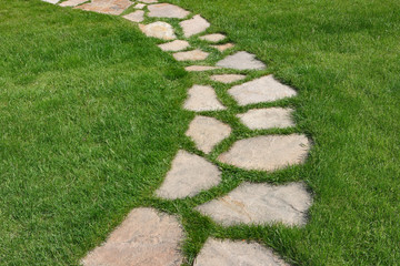 Stone path on a green grassy lawn. The way paved single stones among a green grass.