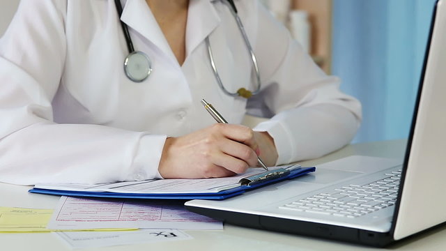 Woman doctor working in office, writing down medical records, filling out papers