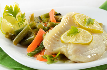 Tilapia fish baked with herbs and lime served on white plate wit