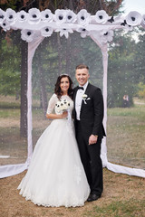 bride and groom stand near arch at wedding ceremony