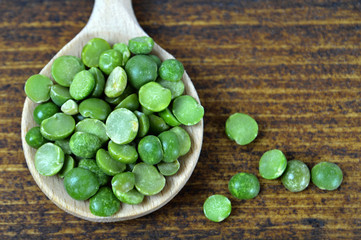 Green lentil beans in wooden spoon on wooden background, top view