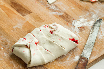 Raw puff pastry on cutting board, filled with red fruit sauce. Ready for baking.