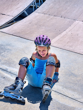 Girl in roller skates falling on ride in skatepark.