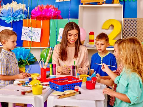Kids with young teacher woman painting on paper at big table  together in  kindergarten . 