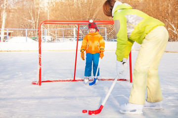 Fototapeta premium Mom and boy play ice hockey outside on playground