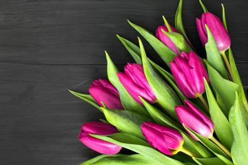Bukiet różowych tulipanów leżący na czarnych deskach. 