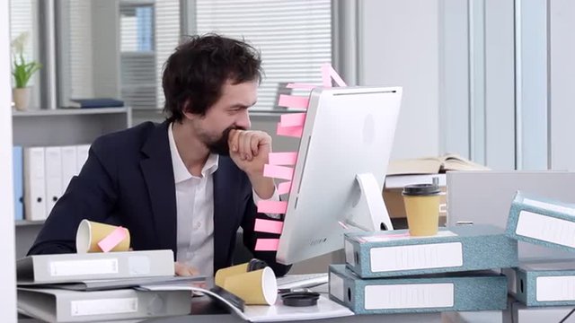Too Many Task For Me/Businessman sits on a workplace beside a computer. He's in a bad mood, he is angry and embarrassed
