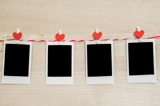 4 Blank instant photo and red clip paper heart hanging on the clothesline with wood background.Designer concept.