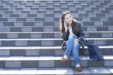 Young woman with sunglasses is talking on the phone sitting on the stairs