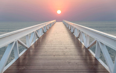 The bridge leads to the sea during sunset.