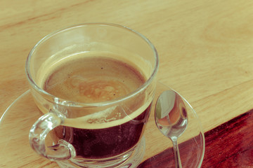 Black expresso coffee in small glass cup on wooden table with teaspoon, vintage style