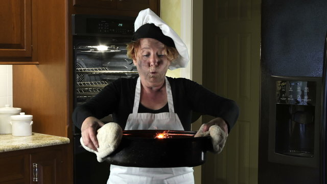 Woman wearing apron and chefs hat holding burning roasting pan.