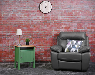 Brown leather armchair and green small table against brick wall background