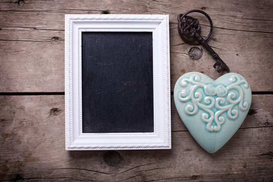 Turquoise  decorative  heart, empty blackboard and vintage key on aged wooden background. Selective focus. Place for text.