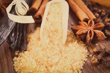 Vintage photo, Brown sugar cane on spoon, fresh fragrant vanilla pods and cinnamon sticks, star anise and cloves on wooden surface plank, seasoning for cooking or baking