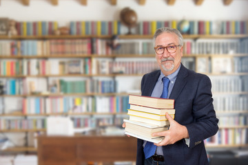 Senior teacher standing holding a book in front of a bookcase