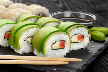 Sushi rolls with avocado, salmon and sesame seeds on slate tray.