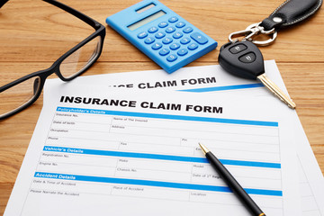 Insurance claim form with pen and car key on wood desk